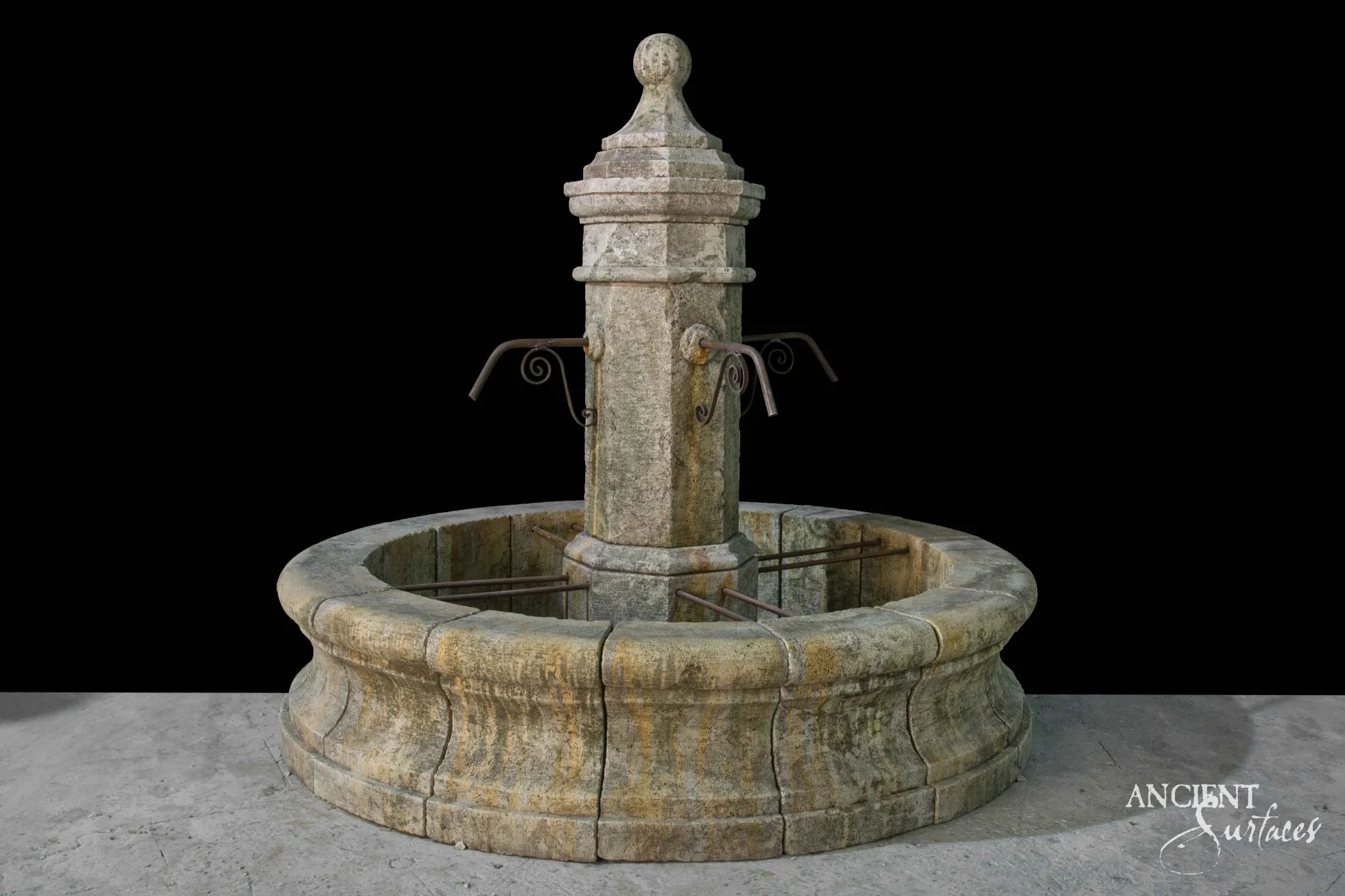 Reclaimed antique limestone pool fountain from Ancient Surfaces with a tall octagonal pillar, stepped cap and ball finial, two rusted iron scroll spouts, and a round basin streaked with ochre and green water staining