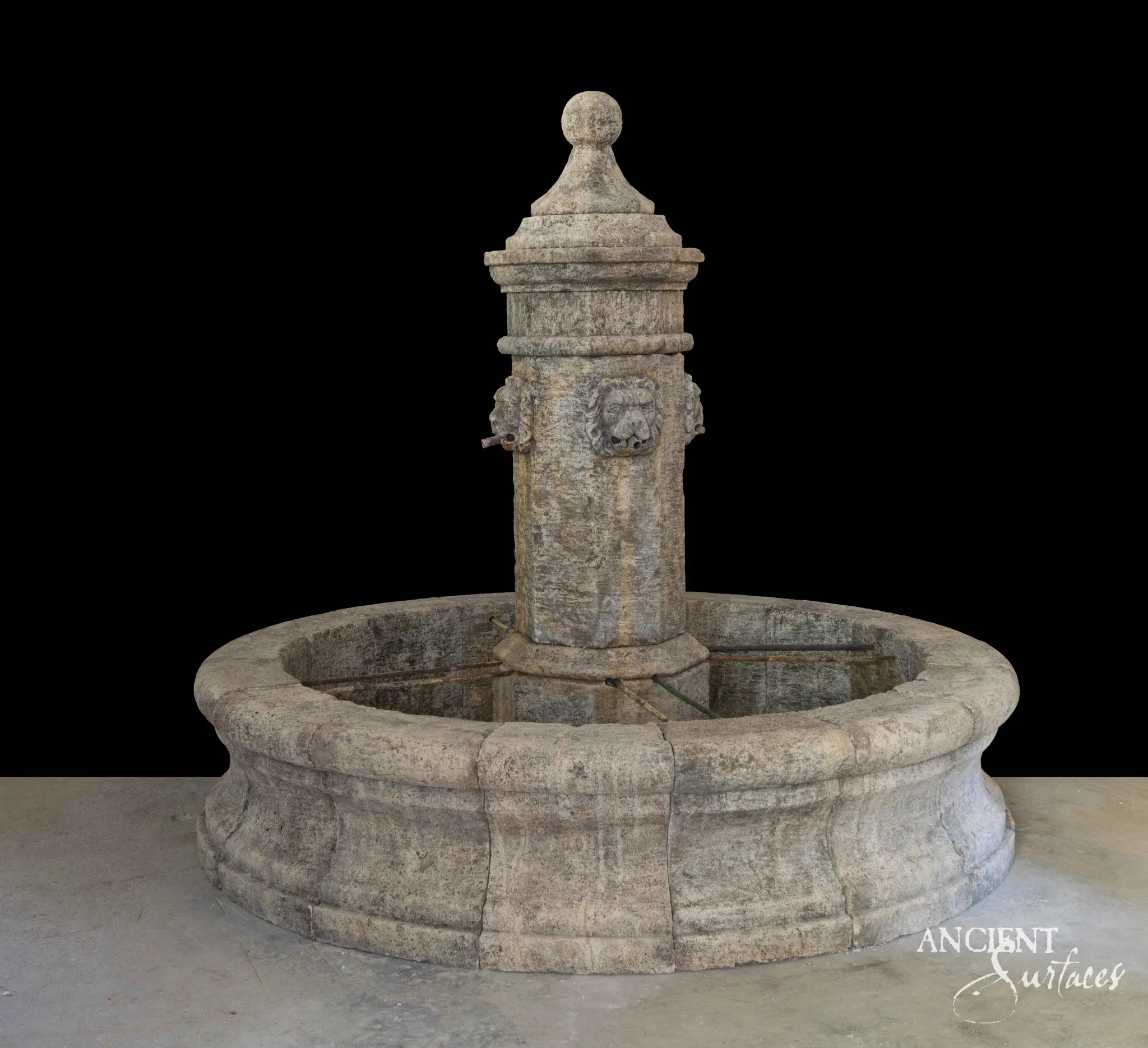 Reclaimed antique limestone pool fountain from Ancient Surfaces with a cylindrical column carrying a carved lion mascaron and two smaller side masks with metal spouts, under a ball finial, in a round panelled basin