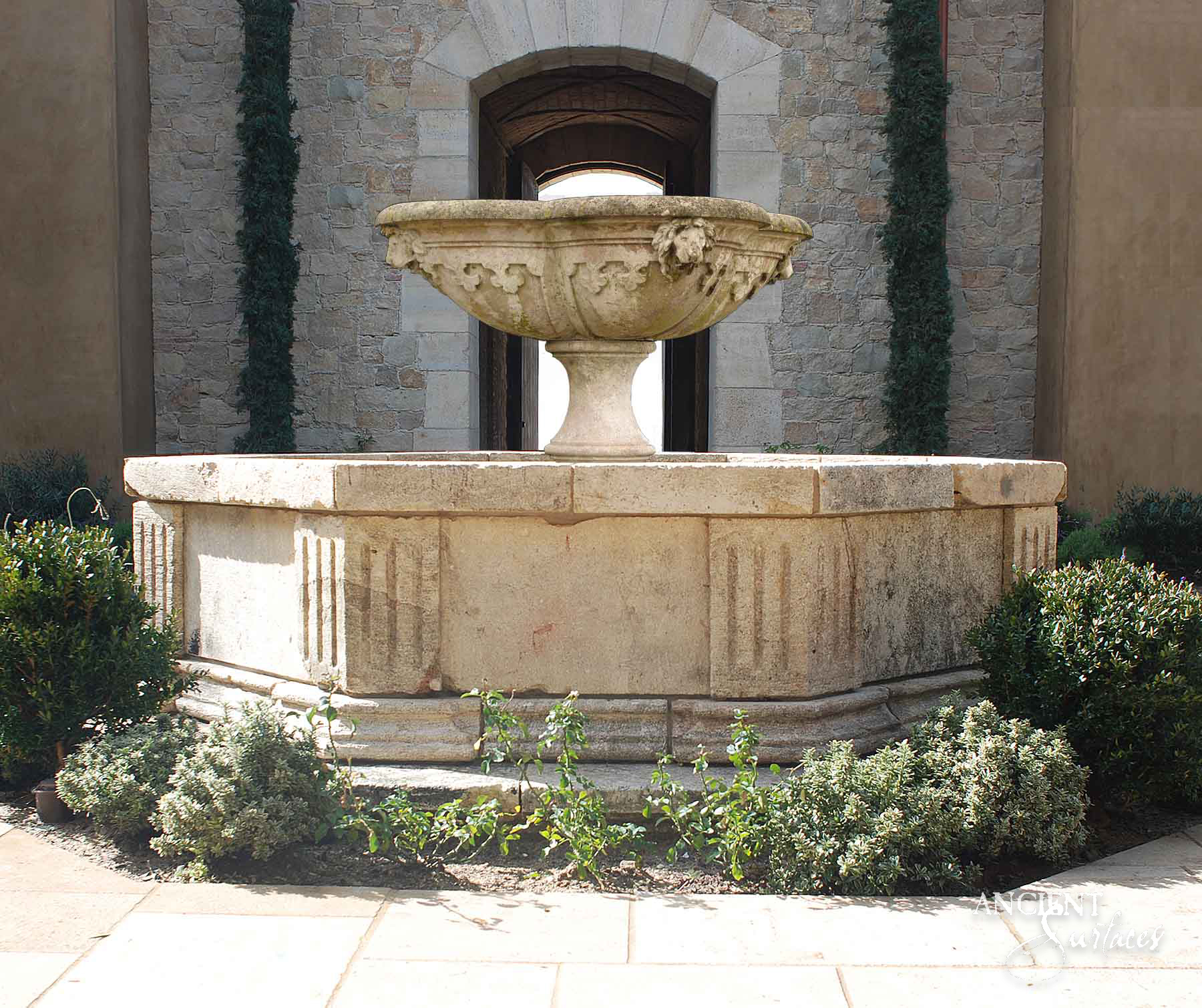 Large octagonal reclaimed antique limestone pool fountain from Ancient Surfaces in a stone courtyard, the pool wall panelled with fluted pilasters and a carved tazza bowl with a lion mask at its centre