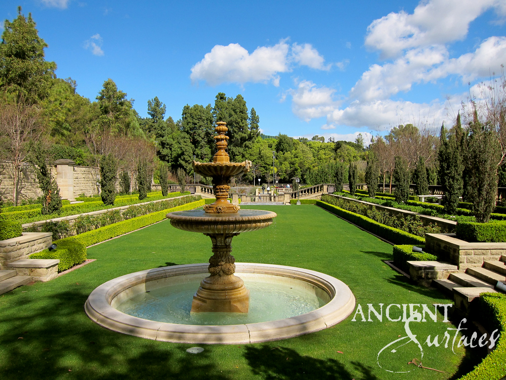 Reclaimed antique limestone two tier pool fountain from Ancient Surfaces running at the centre of a wide shallow circular pool set into an estate lawn, its gadrooned bowls carried on a carved baluster stem